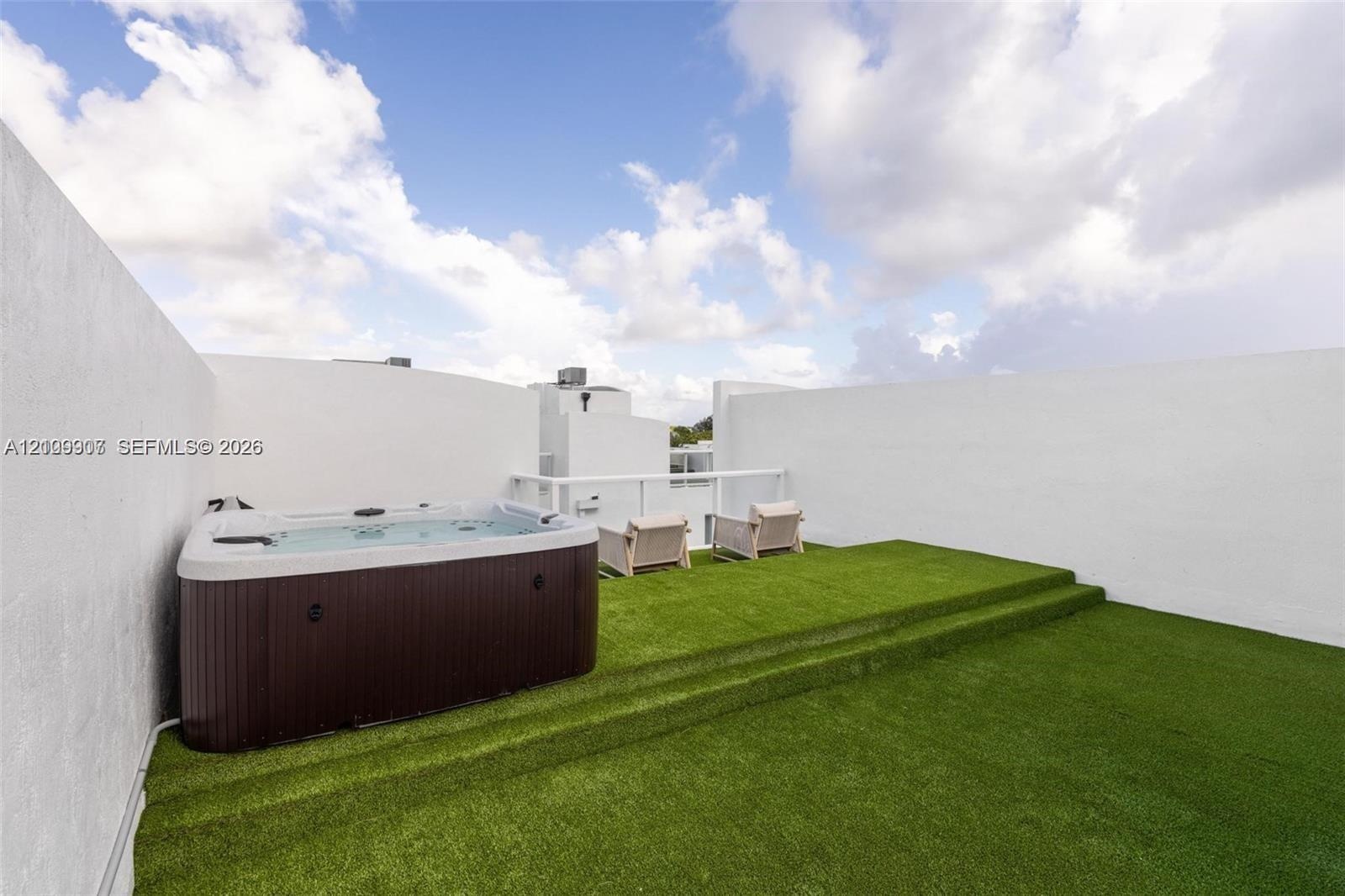 Rooftop terrace featuring synthetic grass surfacing, tiered platform levels, high perimeter walls for privacy, and a built-in spa