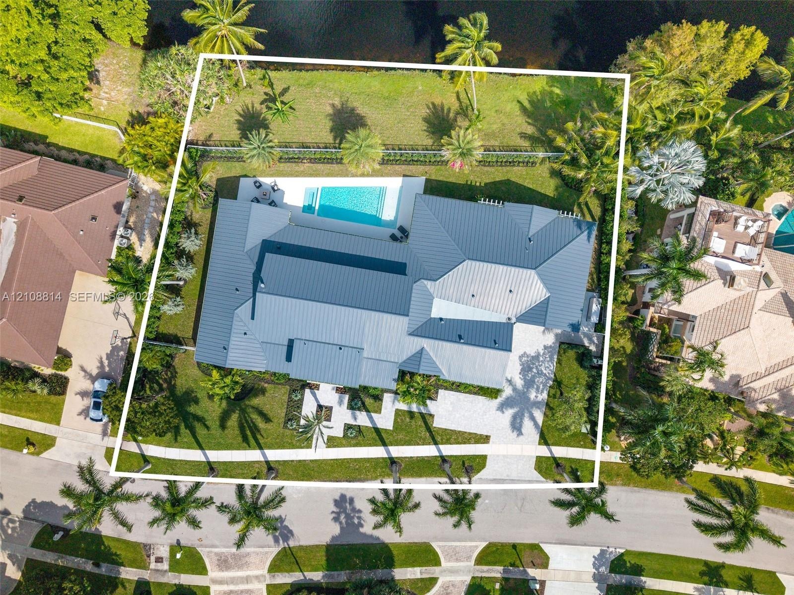 Aerial view of a residential property featuring a metal roof, an in-ground swimming pool, a paver driveway, and mature landscaping