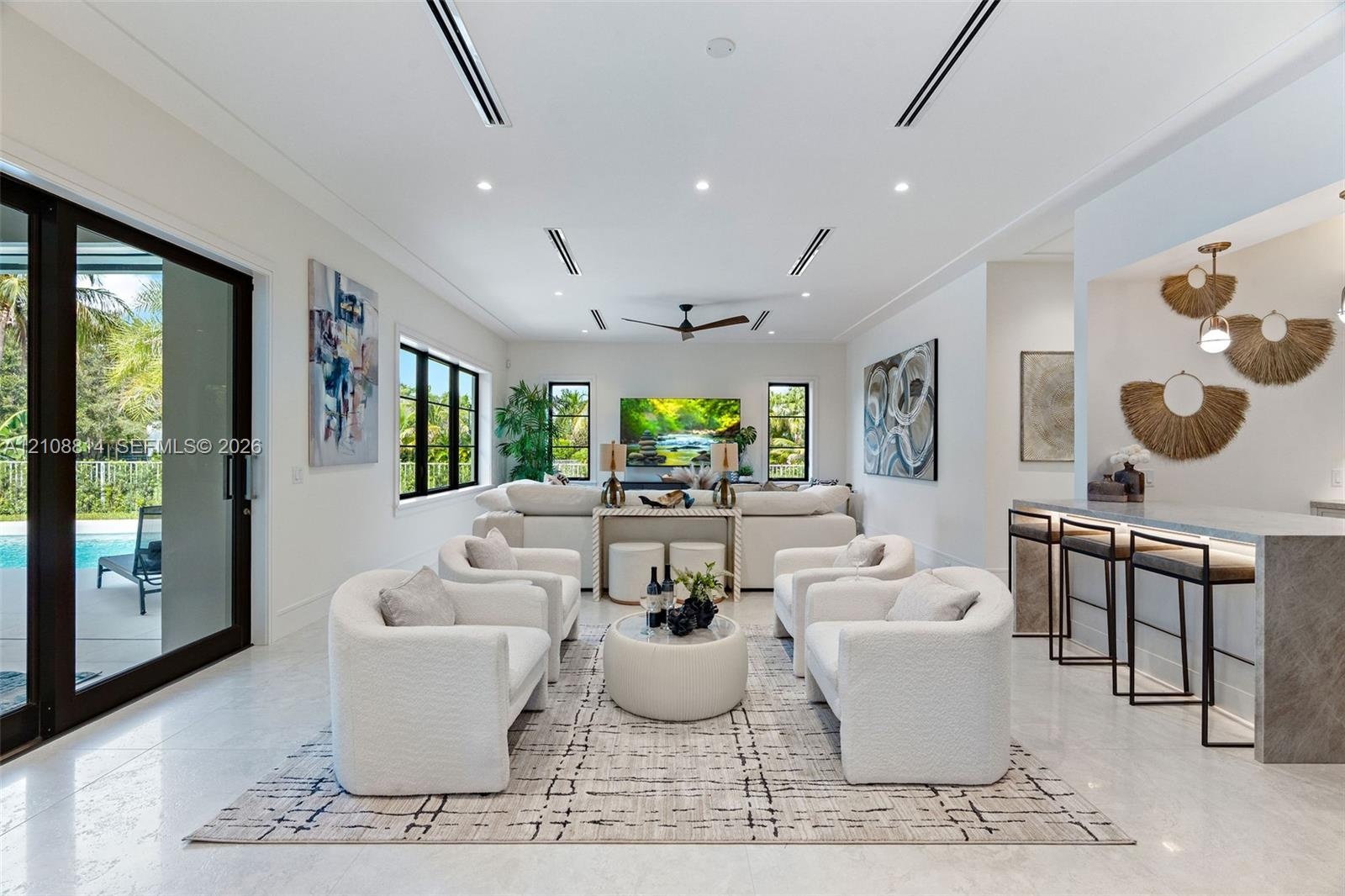 Open-concept living area featuring large-format stone flooring, recessed linear lighting, black-framed windows, integrated wet bar with stone countert