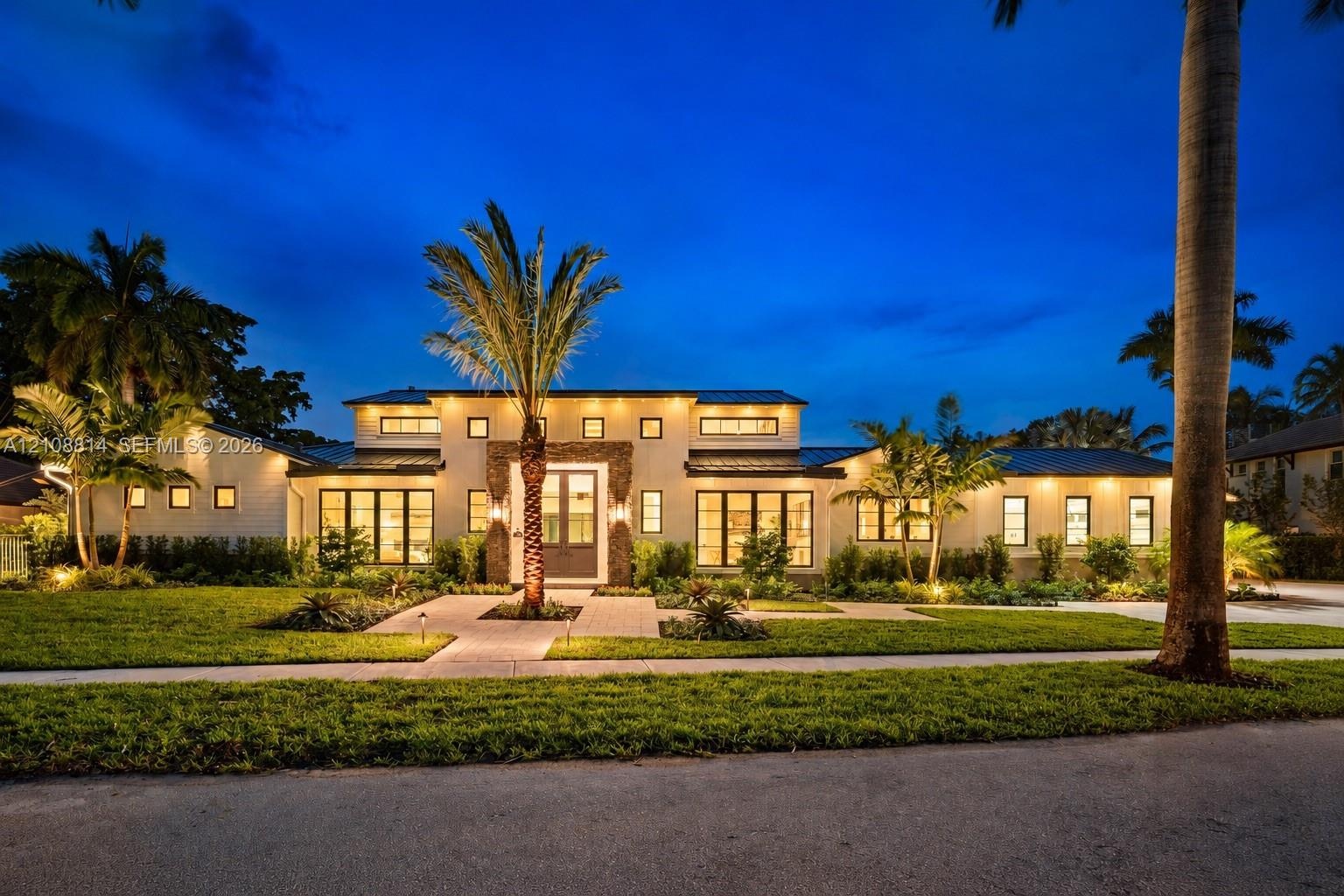 Single-story residence featuring light-toned stucco exterior, stacked stone facade accents, dark metal roof, multiple transom windows, and paved stone