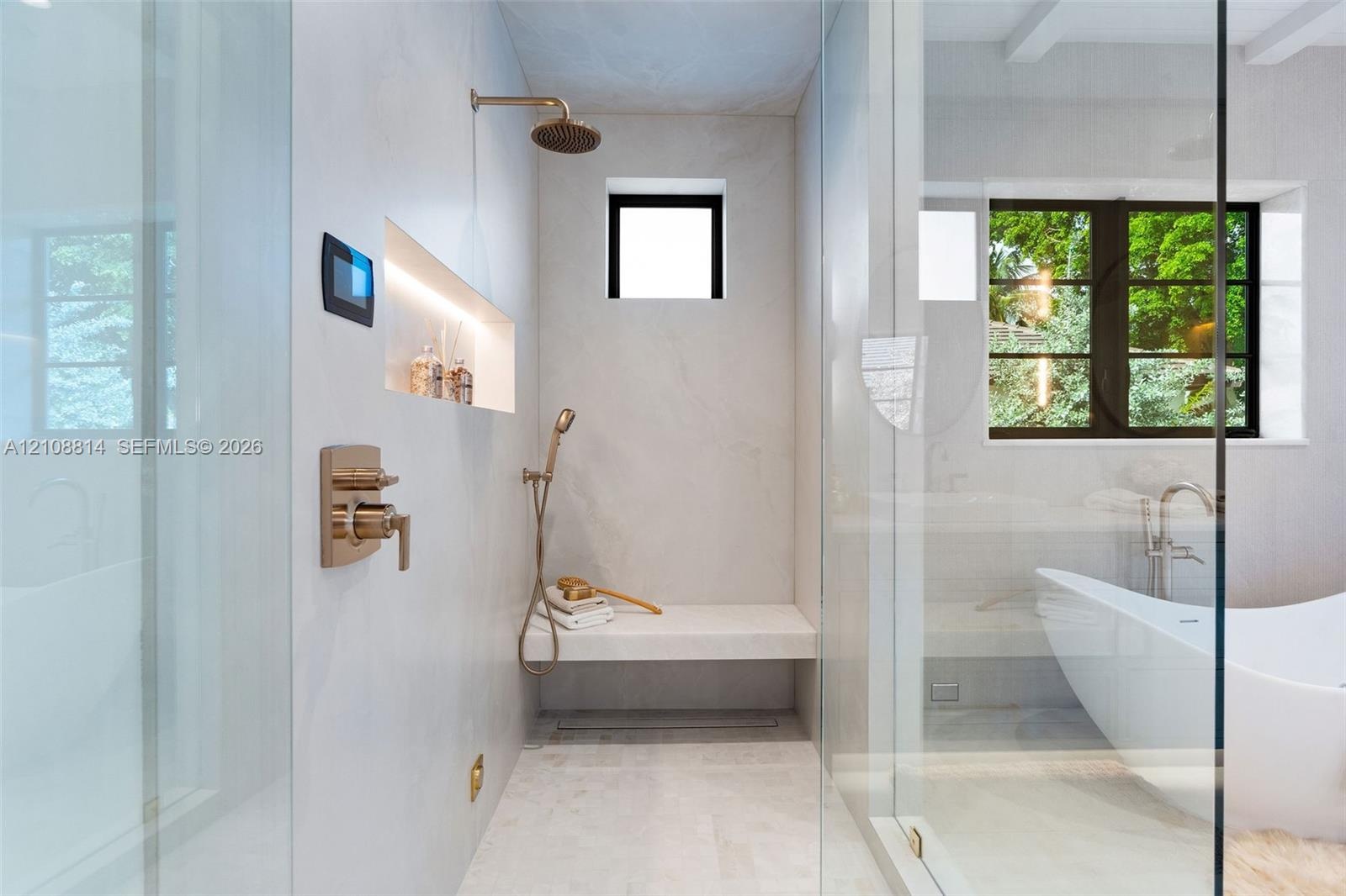 Walk-in shower featuring a built-in stone bench, rain showerhead with handheld sprayer, recessed shelving with integrated lighting, digital control in