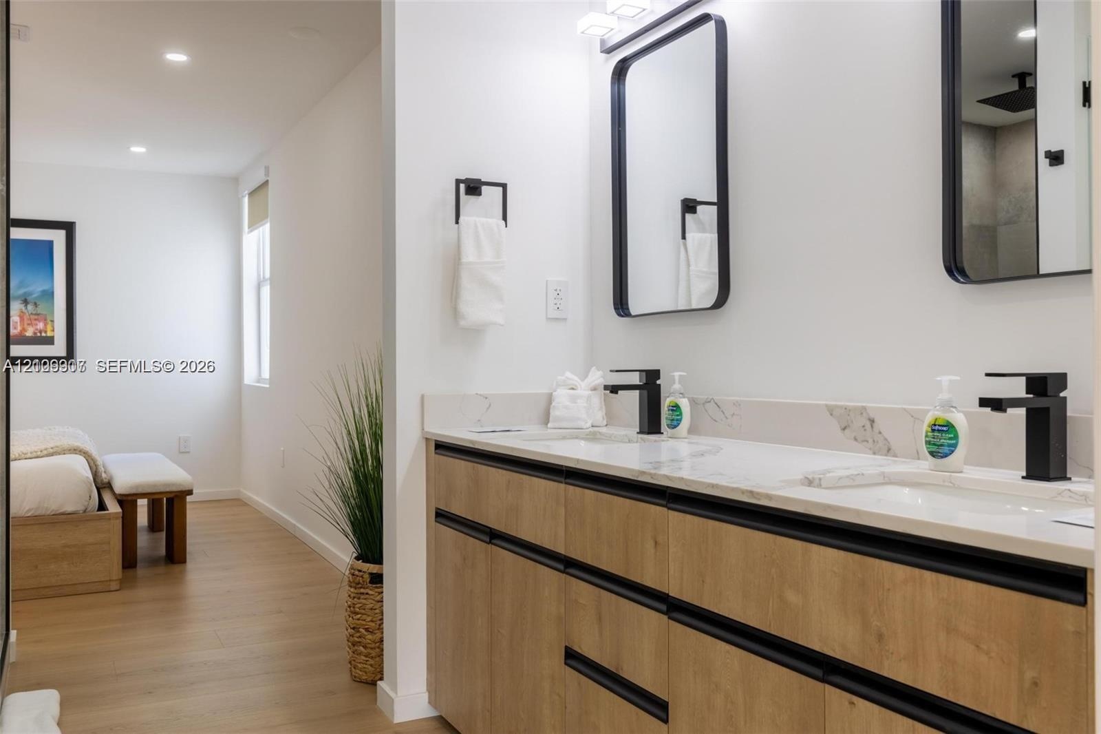 Modern vanity with wood-finish cabinetry, dual undermount sinks, stone-finish countertops, matte black fixtures, and rectangular mirrors