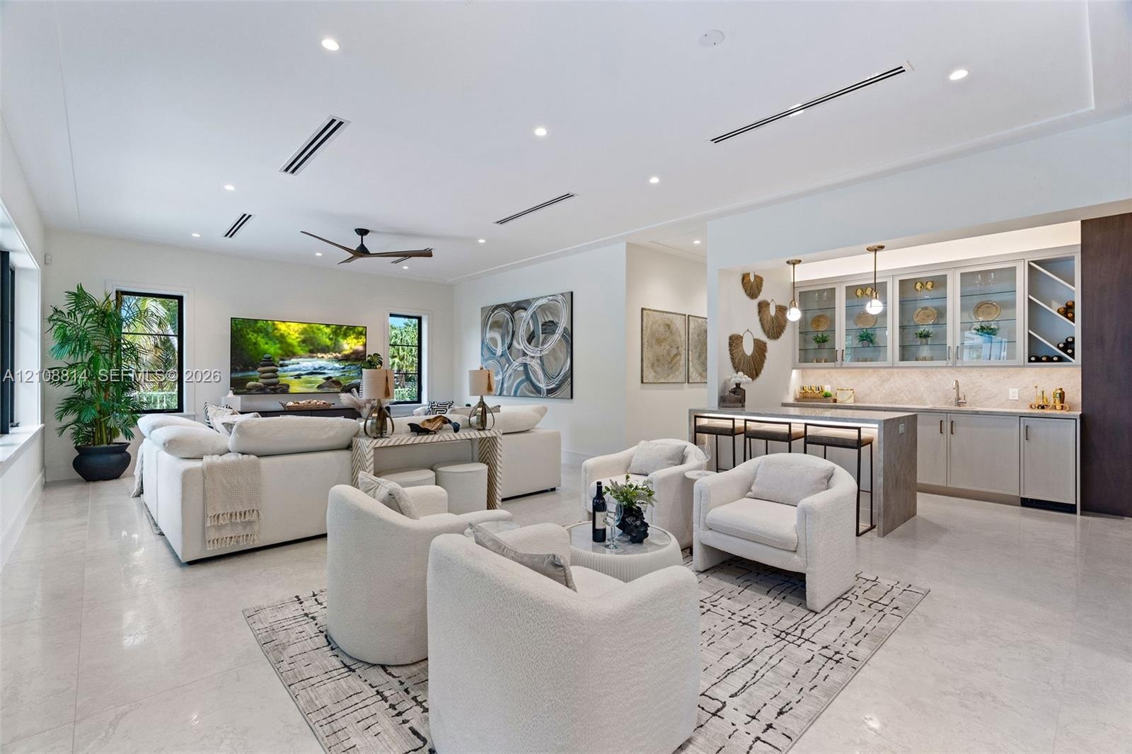 Open-concept living space featuring high ceilings with recessed lighting, large-format tile flooring, a dedicated wet bar with glass-front cabinetry, 