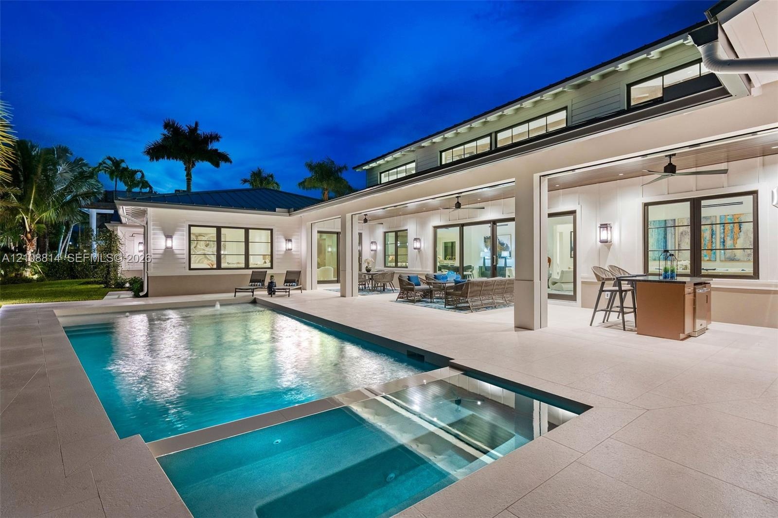 Covered outdoor patio with stone tile flooring, built-in outdoor kitchen, swimming pool with integrated spa, and expansive multi-panel sliding glass d
