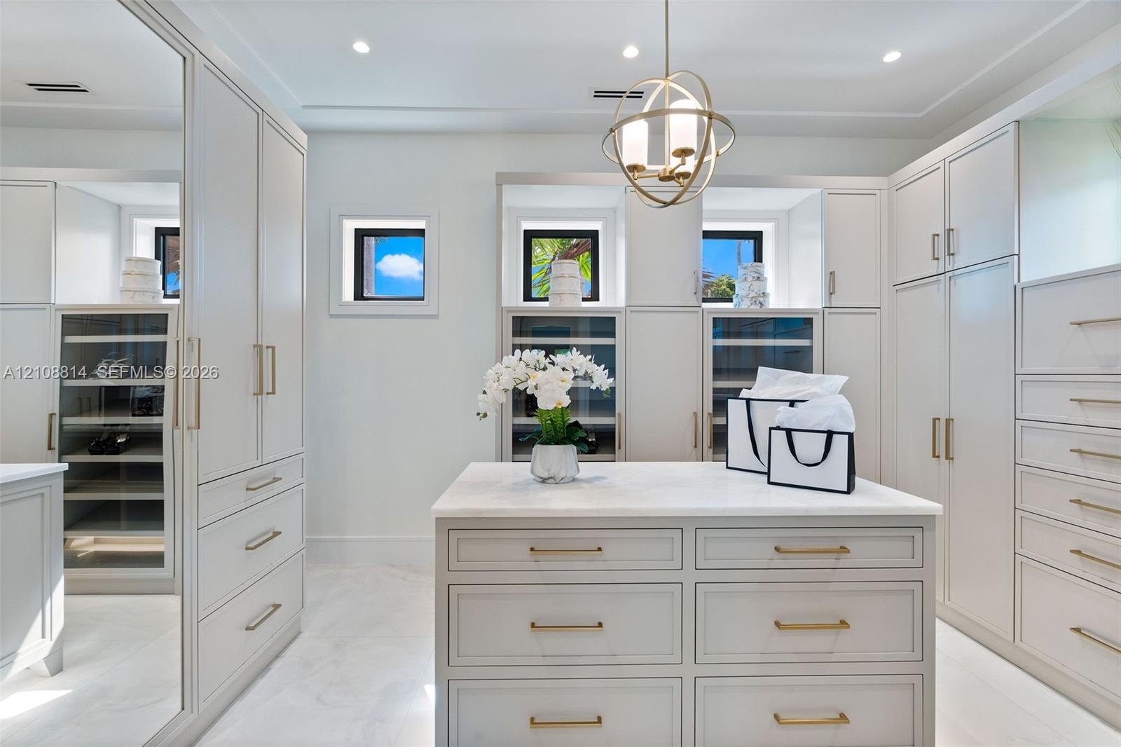 Custom cabinetry featuring glass-front display doors and integrated shelving, central storage island with stone-finish countertop, brushed brass hardw
