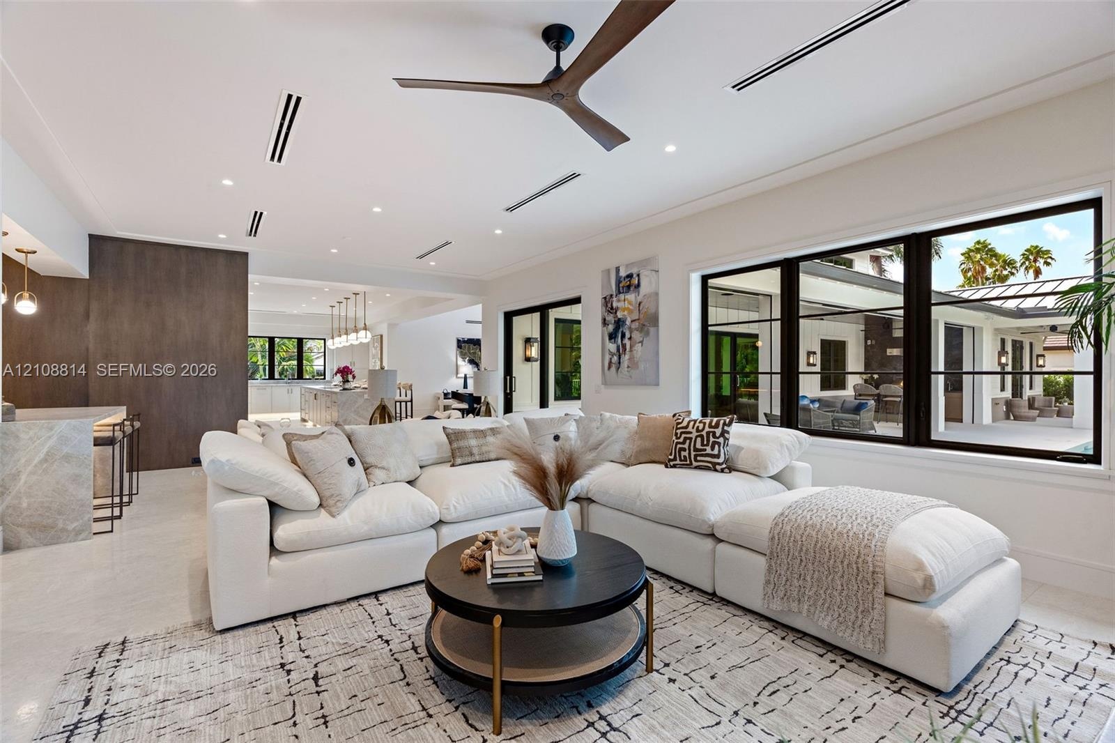 Open-concept living space featuring high ceilings with recessed lighting, a modern ceiling fan, expansive black-framed windows, and light-toned floori