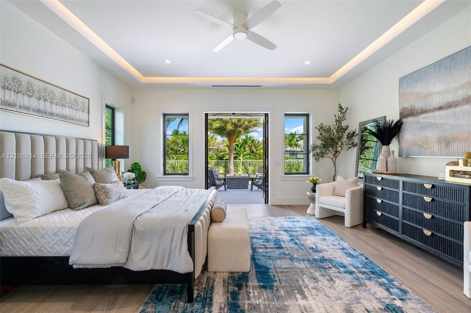 Bedroom featuring a tray ceiling with cove lighting, porcelain-finish flooring, a ceiling fan, and multi-pane windows with glass door access to an ext