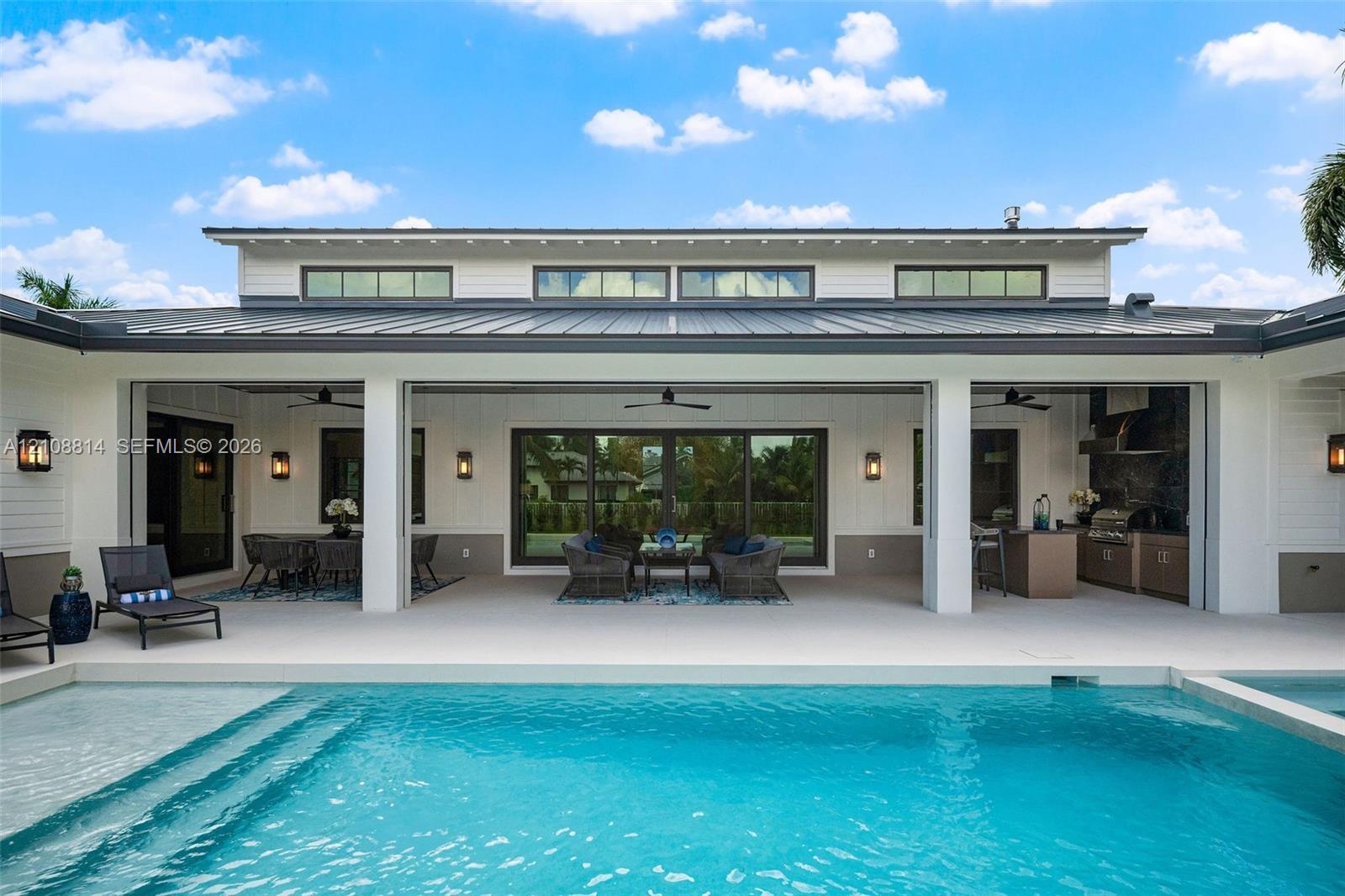Covered lanai featuring an outdoor kitchen with built-in cabinetry, clerestory windows, metal roofing, and a swimming pool