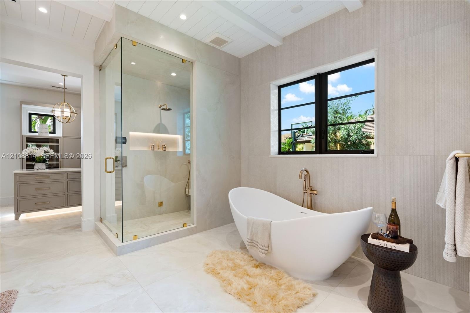 Freestanding soaking tub with a wall-mounted faucet, glass-enclosed shower featuring built-in shelving, large-format tile flooring, and plank-style ce