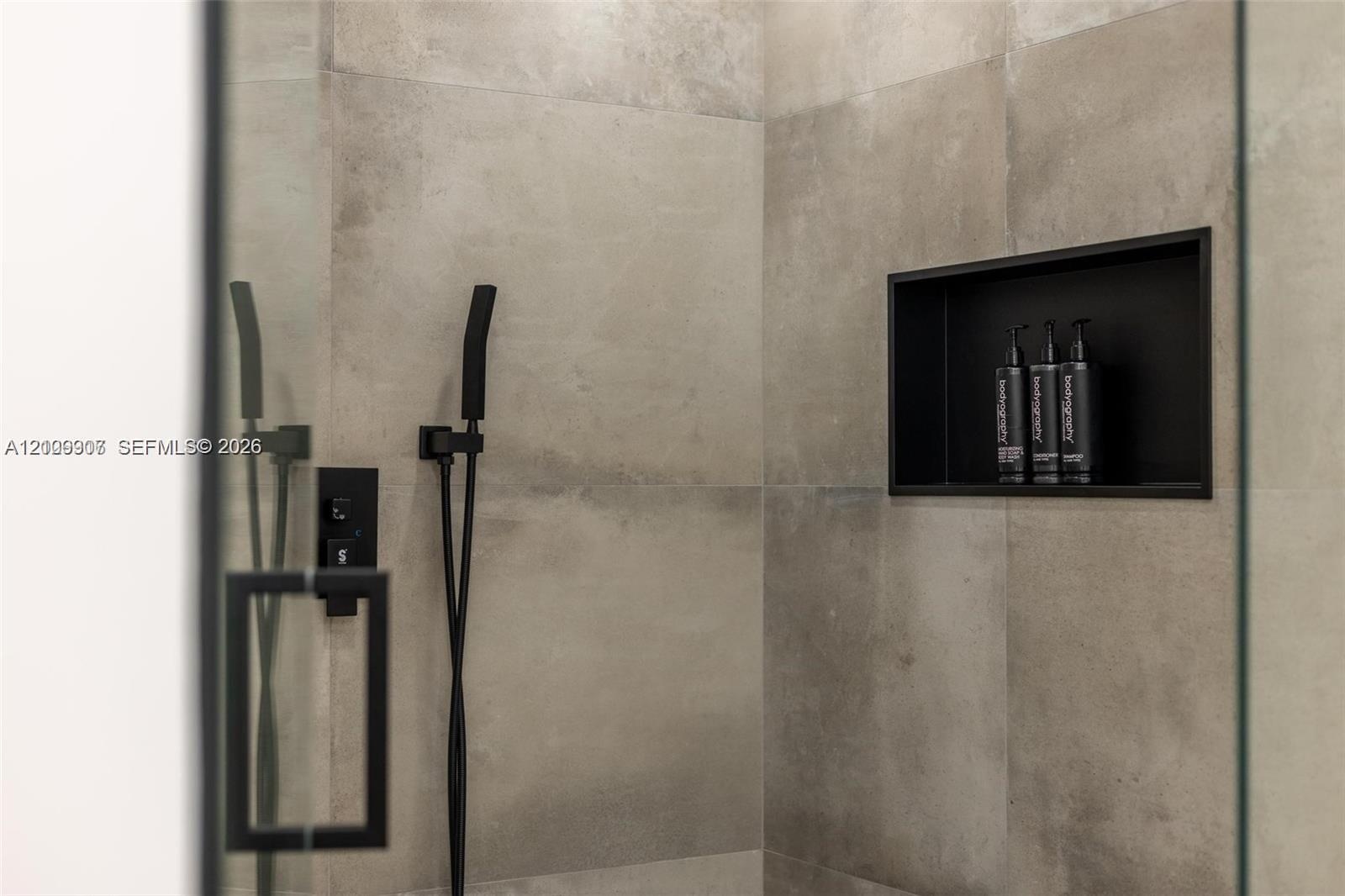 Shower enclosure featuring large-format grey tile, matte black shower hardware, a hand-held shower sprayer, and a built-in recessed storage niche