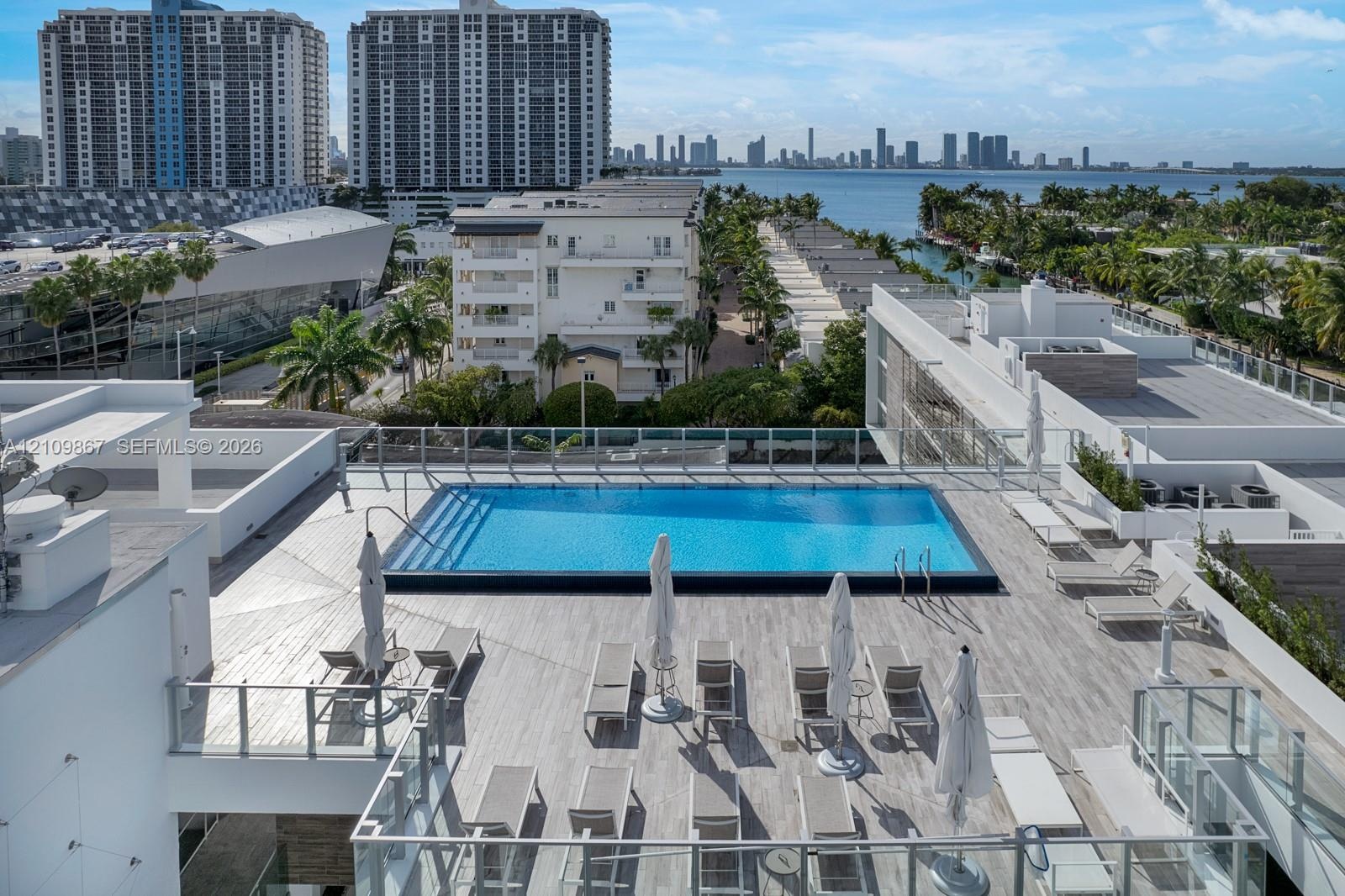 Rooftop terrace featuring a rectangular swimming pool, expansive stone-tile decking, and glass panel railing