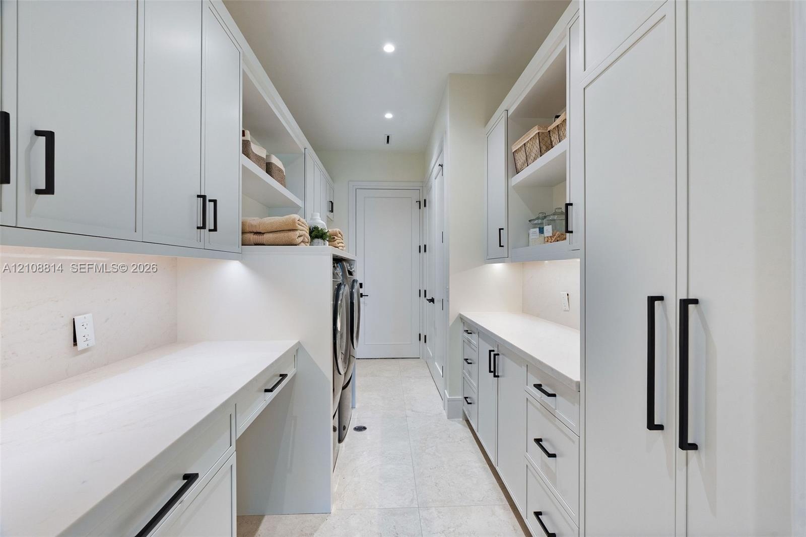 Custom cabinetry with matte black hardware, stone countertops, integrated under-cabinet lighting, and light-toned tile flooring