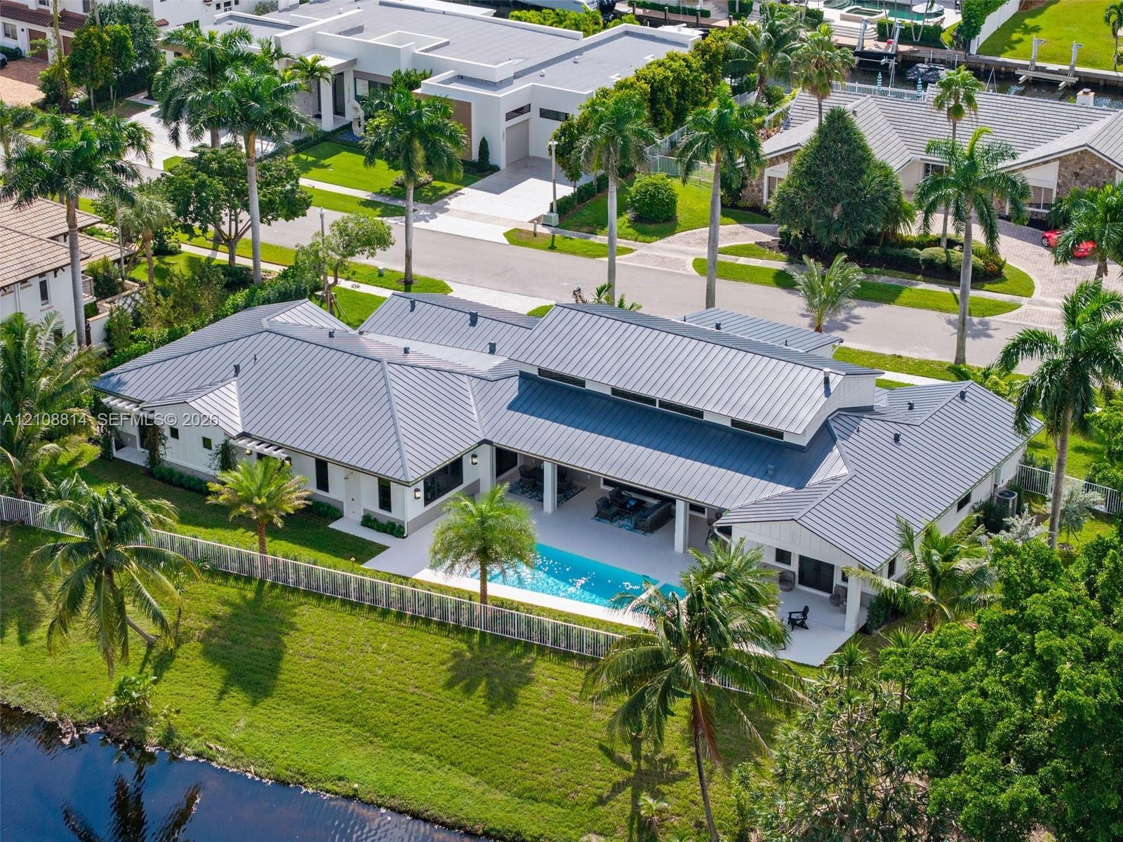 Single-story residence featuring a metal roof, rear swimming pool, covered patio, white exterior finish, and waterfront lot