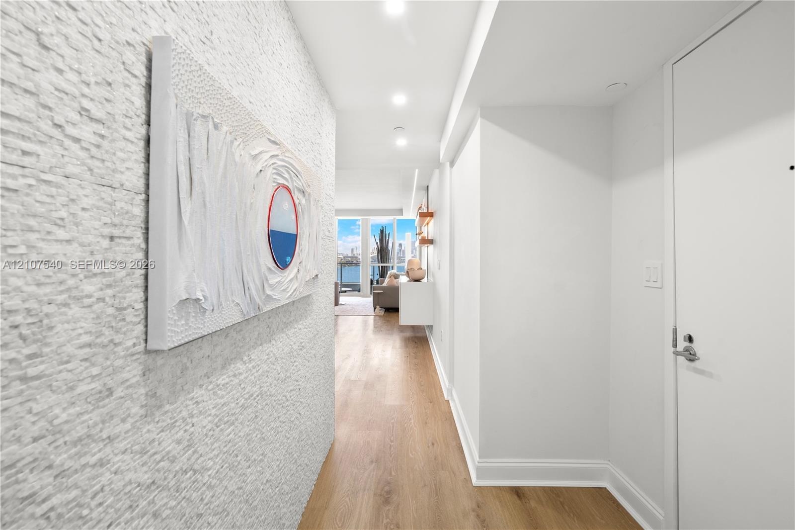 Textured stone accent wall, wood-finish flooring, recessed lighting, and expansive floor-to-ceiling windows