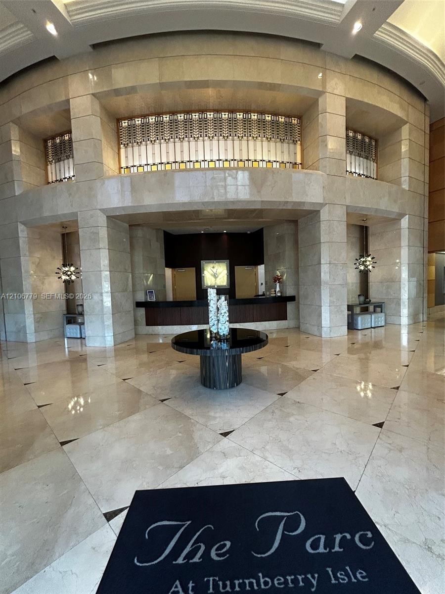 Grand lobby featuring floor-to-ceiling stone wall cladding, polished stone tile flooring with decorative inlay, a multi-level architectural recessed f