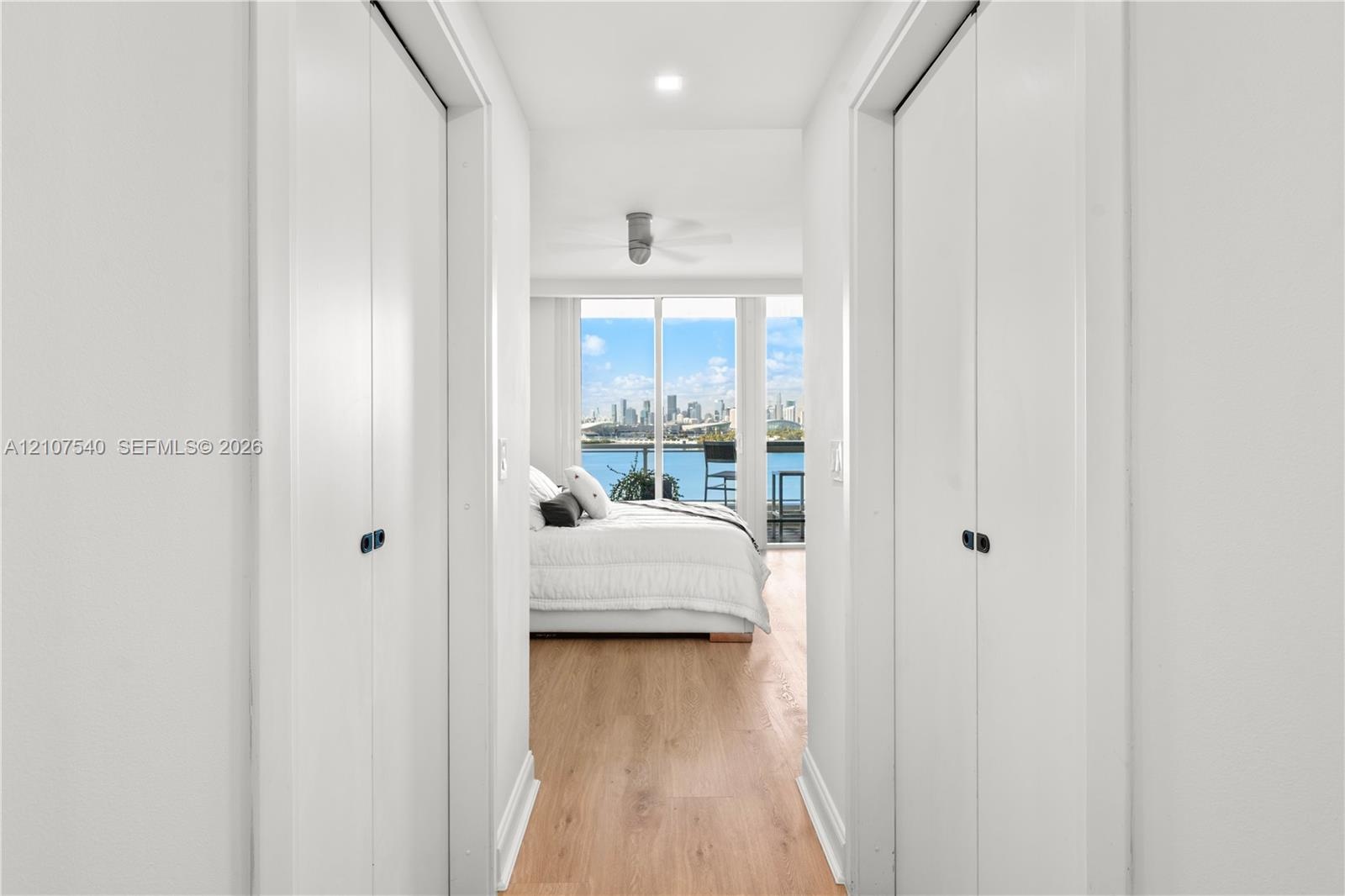 Master bedroom hallway with dual bifold closet doors, wood-finish flooring, recessed LED lighting, and floor-to-ceiling windows with views of the down