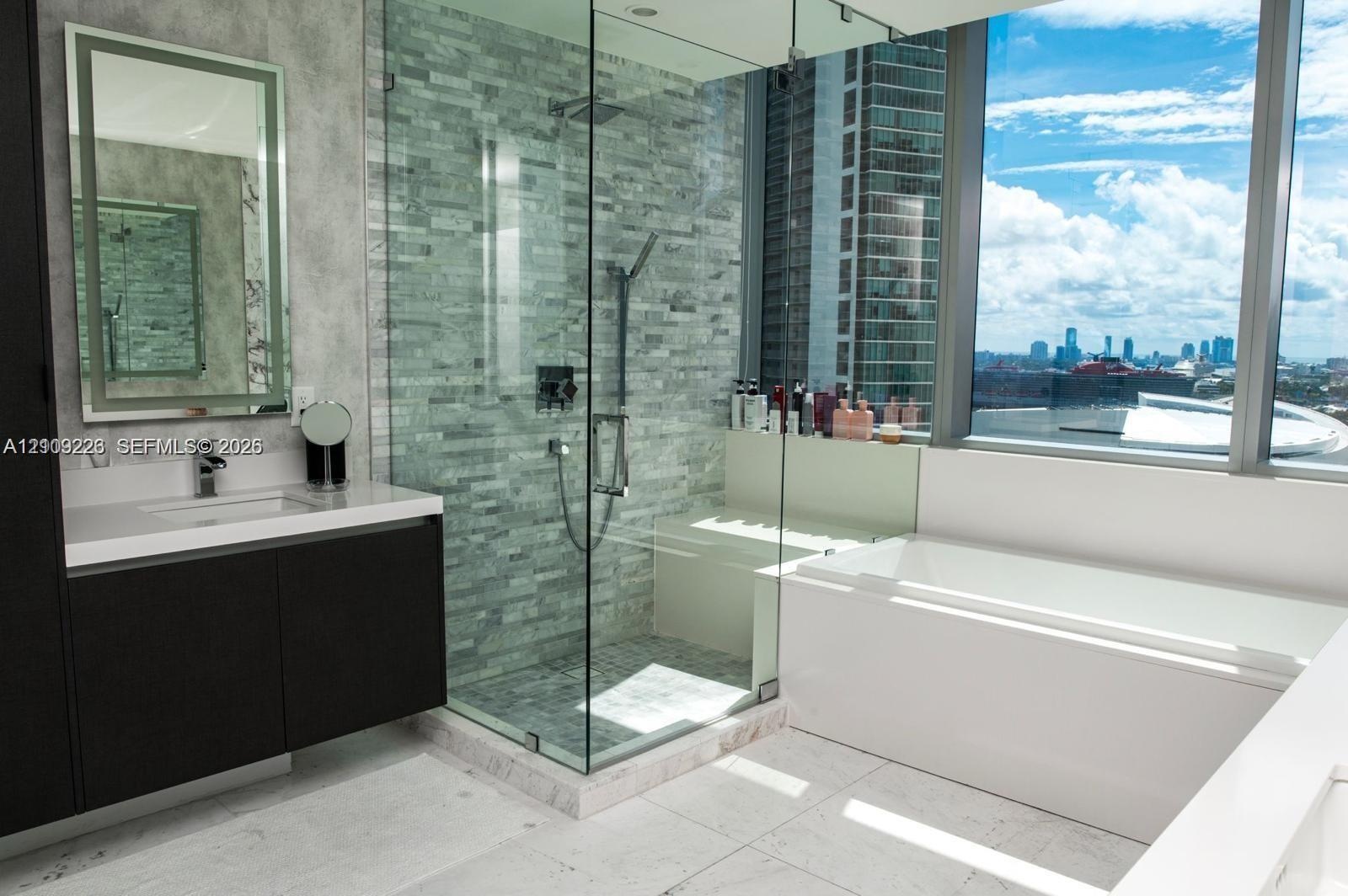 Modern floating vanity with a stone countertop, floor-to-ceiling glass-enclosed shower featuring stone wall tile and an integrated bench, deep soaking