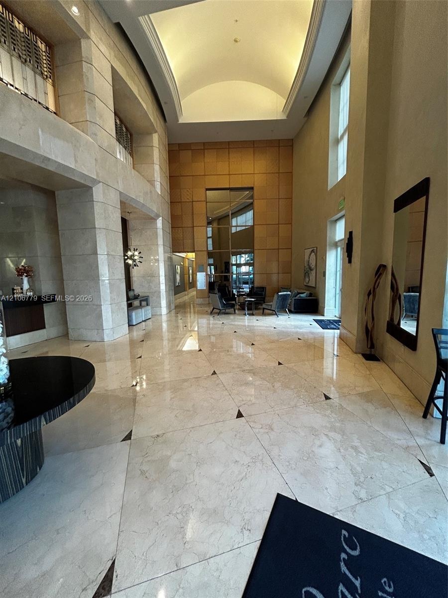 Grand lobby featuring polished stone flooring with geometric insets, expansive multi-story ceilings, large-scale stone-clad pillars, and a decorative 