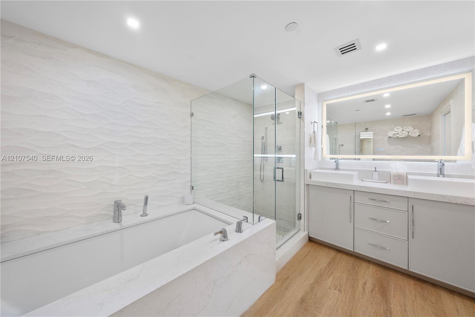 Master bathroom featuring a frameless glass-enclosed shower, a deep soaking tub with stone-finish surround, a dual-sink vanity with comfort height cab