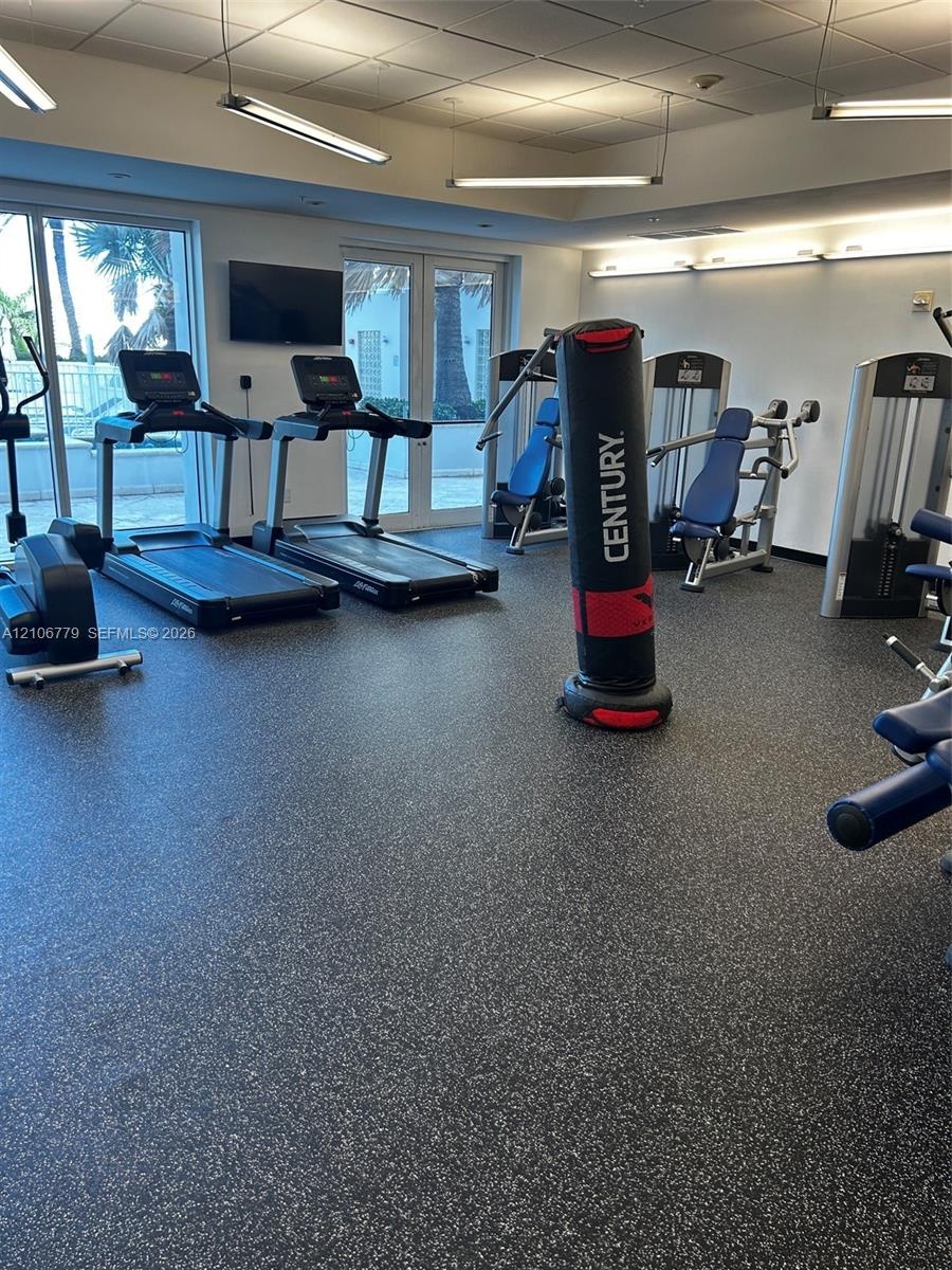 Fitness center featuring durable speckled rubber flooring, suspended linear lighting, and large windows with direct exterior access