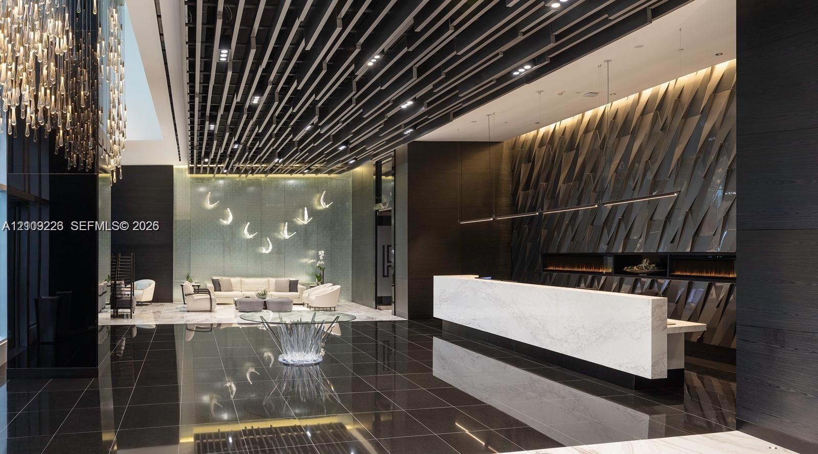 Lobby area featuring a geometric slat ceiling, polished dark tile flooring, a large stone-surface reception desk, a textured feature wall, and integra