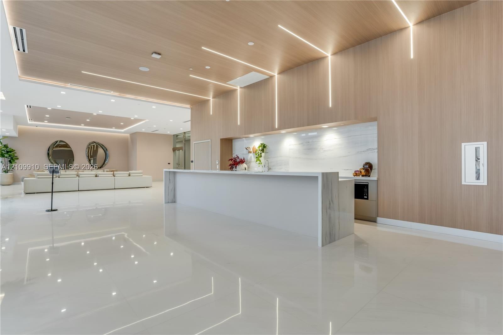 Modern lobby featuring high-gloss tile flooring, floor-to-ceiling wood-finish wall paneling, linear recessed lighting, and a stone-topped reception de