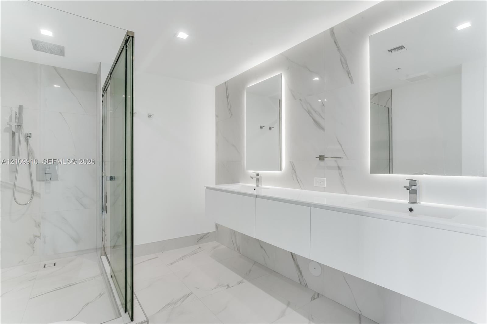 Floating double vanity with dual rectangular sinks, floor-to-ceiling stone-finish tile wall, glass-enclosed walk-in shower with rainfall fixture, and 