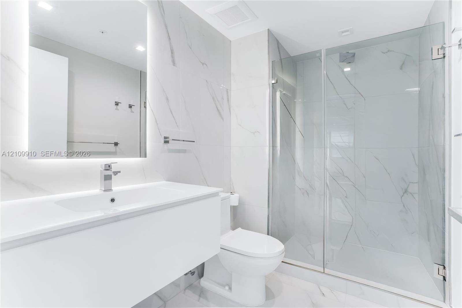 Bathroom featuring a floating vanity with a smooth surface, wall-to-wall mirror with integrated lighting, large-format stone-patterned wall tile, and 