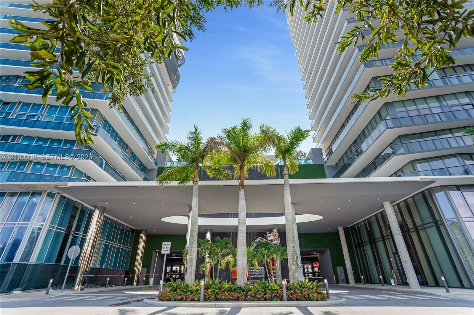 Contemporary high-rise architecture featuring glass facade paneling, covered porte-cochère, recessed lighting, and integrated landscaping with mature 