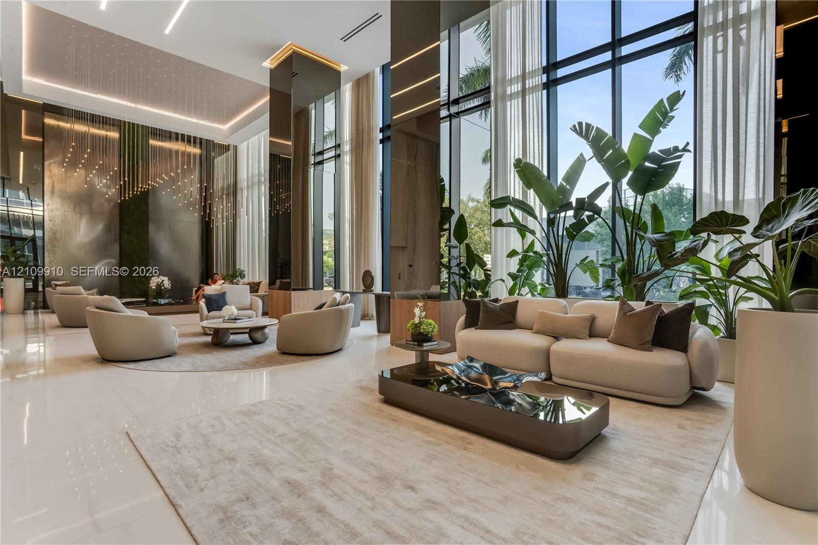Double-height floor-to-ceiling windows, polished stone flooring, recessed ceiling lighting, reflective wall paneling, and architectural metallic accen