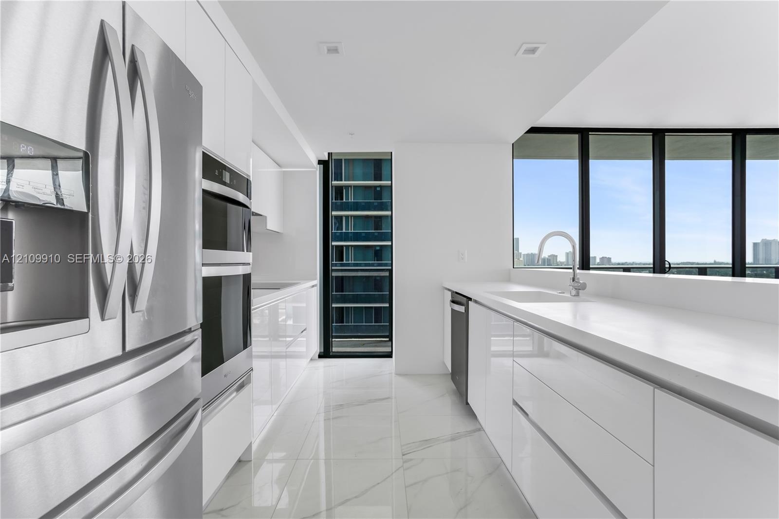 Contemporary kitchen featuring high-gloss cabinetry, stone-finish flooring, quartz countertops, stainless steel appliances, and floor-to-ceiling windo