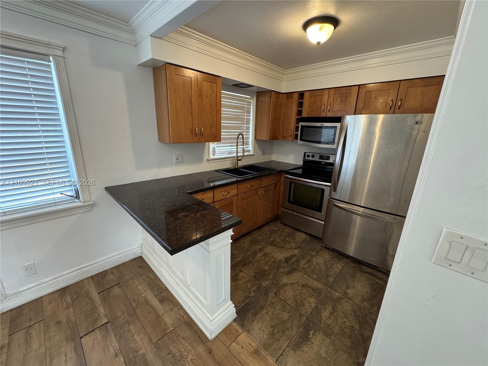 Kitchen featuring wood cabinetry, stone-surface countertops, stainless steel appliances, and multi-format tile flooring