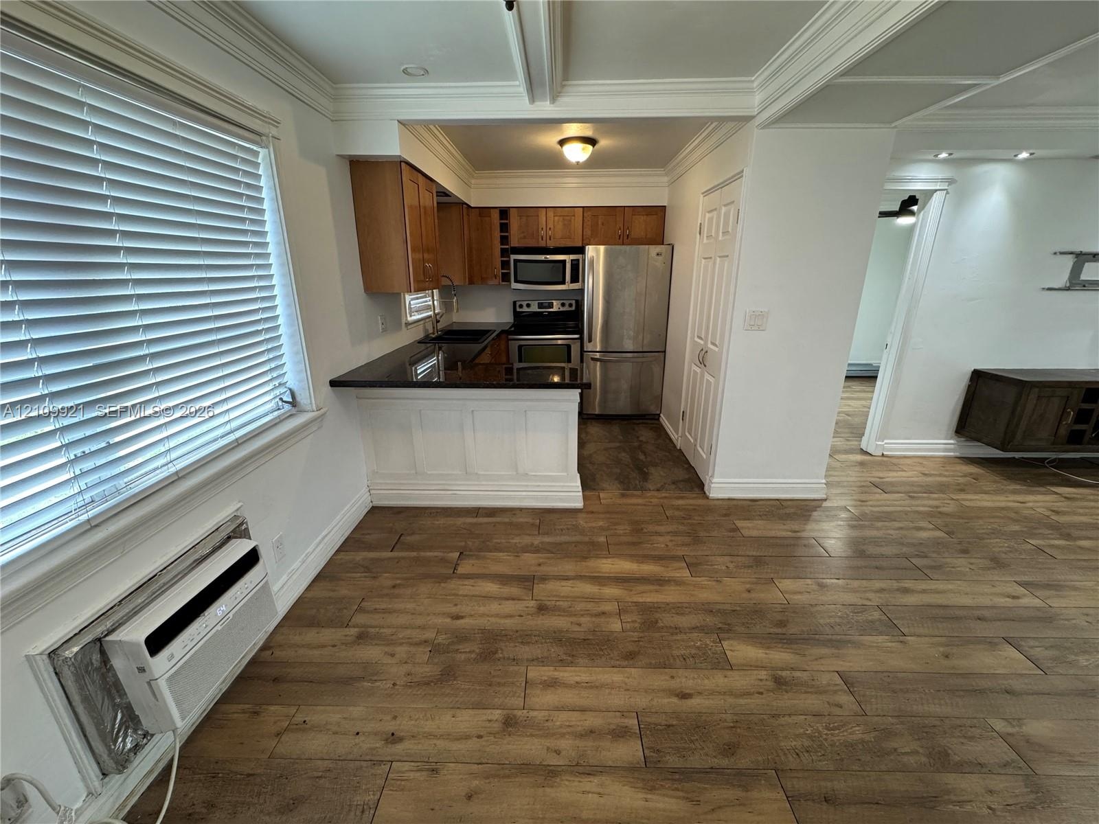 Kitchen featuring wood-finish flooring, dark stone countertops, wood cabinetry, stainless steel appliances, and ceiling crown molding