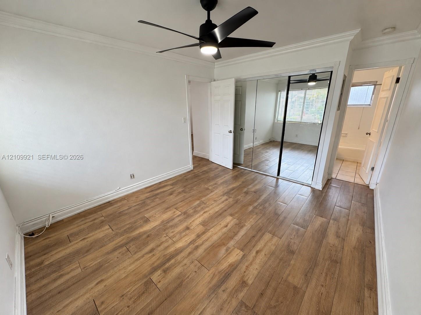 Room featuring wood-finish flooring, a matte black ceiling fan with integrated lighting, crown molding, and floor-to-ceiling mirrored sliding closet d
