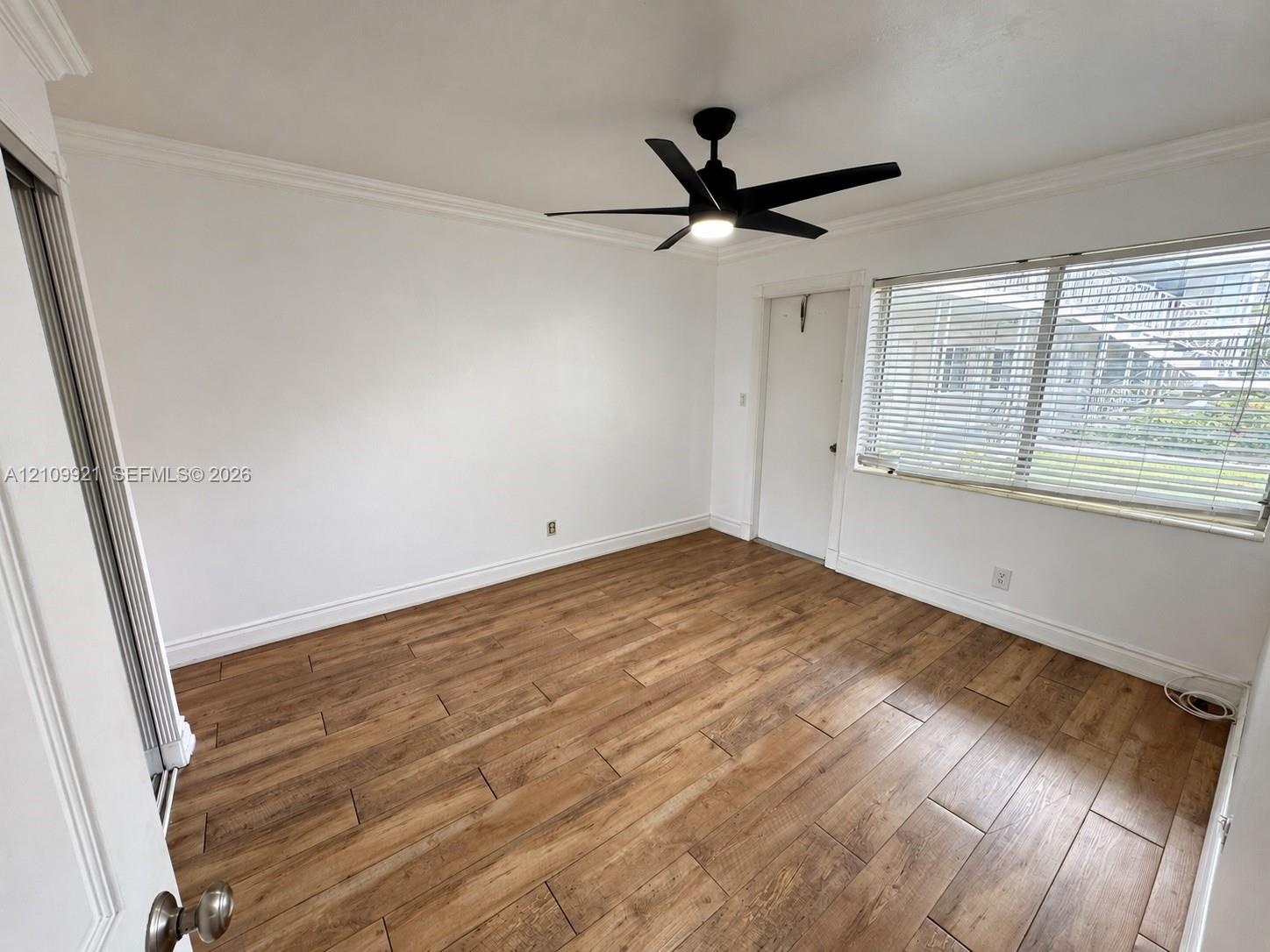Wood-finish tile flooring, neutral walls, crown molding, multi-blade ceiling fan with integrated light, and horizontal window blinds