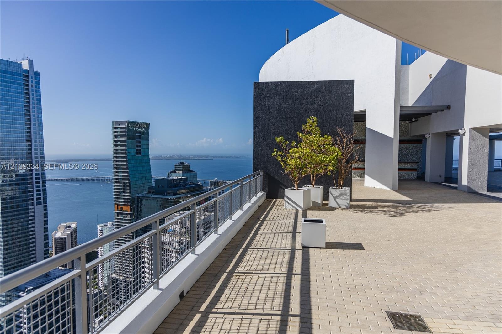 Expansive outdoor terrace featuring paved flooring, a metal safety railing, and high-contrast architectural wall elements