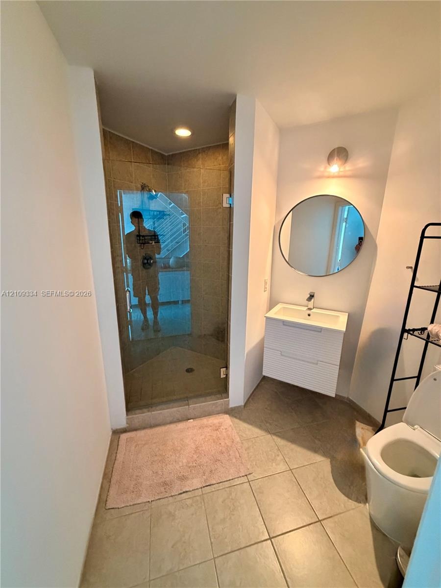 Bathroom featuring a glass-enclosed shower with tiled surround, wall-mounted white vanity with a rectangular sink, circular mirror, and large-format f