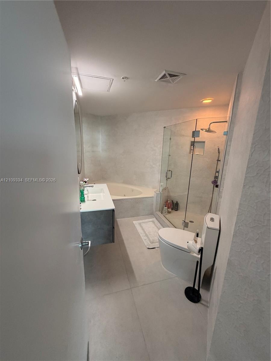 Bathroom featuring a floating vanity with a dual-basin countertop, a glass-enclosed shower, and a soaking tub with stone-finish surround