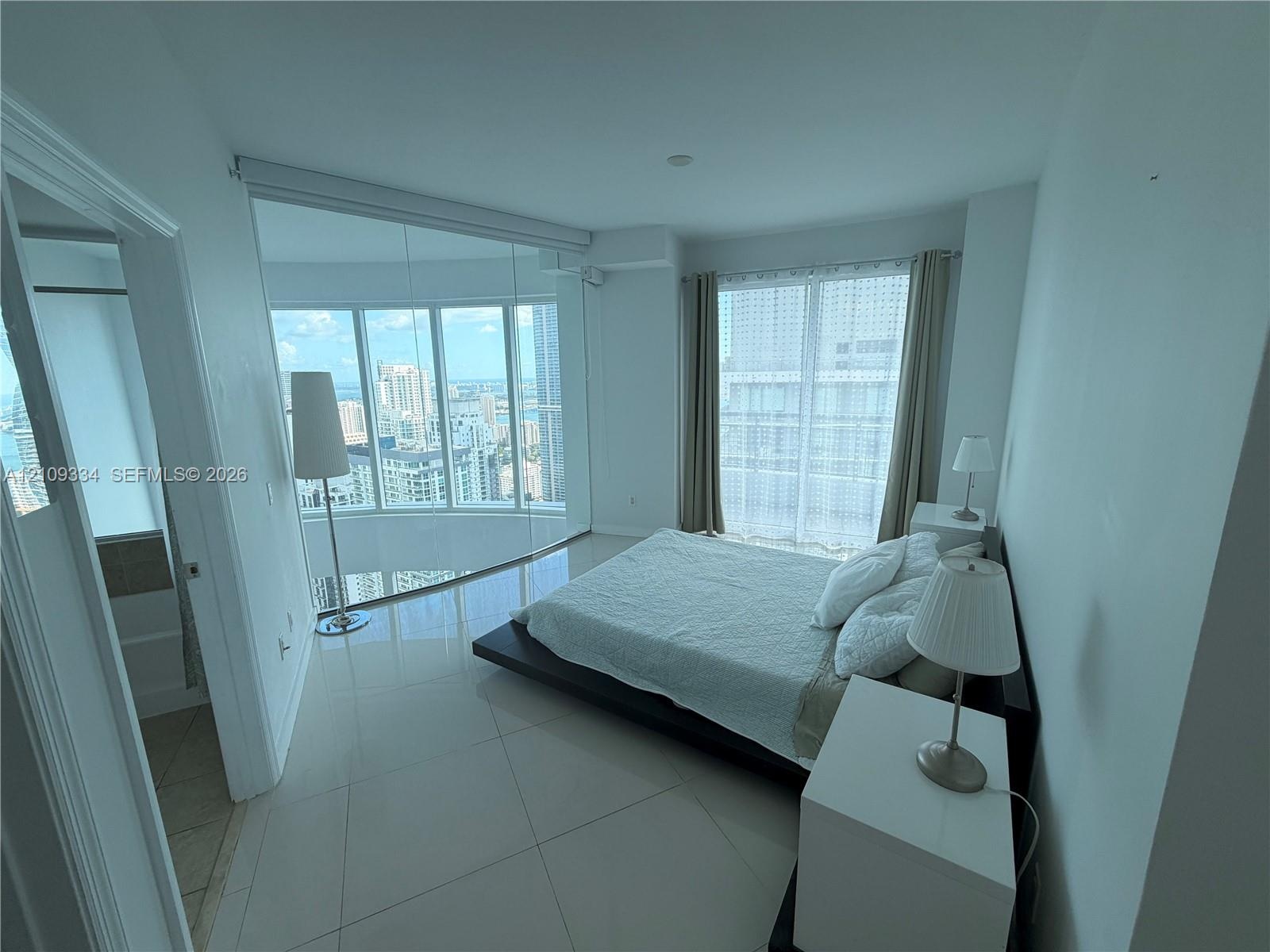 Floor-to-ceiling curved glass windows, expansive ceramic tile flooring, and neutral wall finishes