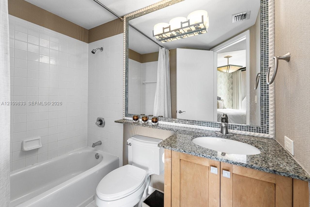 Bathroom featuring a vanity with stone-finish countertop, undermount sink, large mirror with mosaic tile trim, white tile shower surround, and contemp