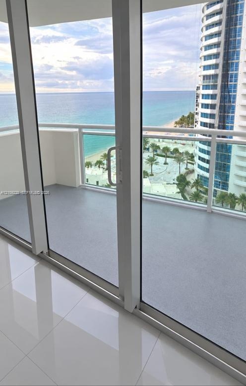 Floor-to-ceiling glass sliding doors opening to a private balcony with a white metal railing, finished with high-gloss tile flooring