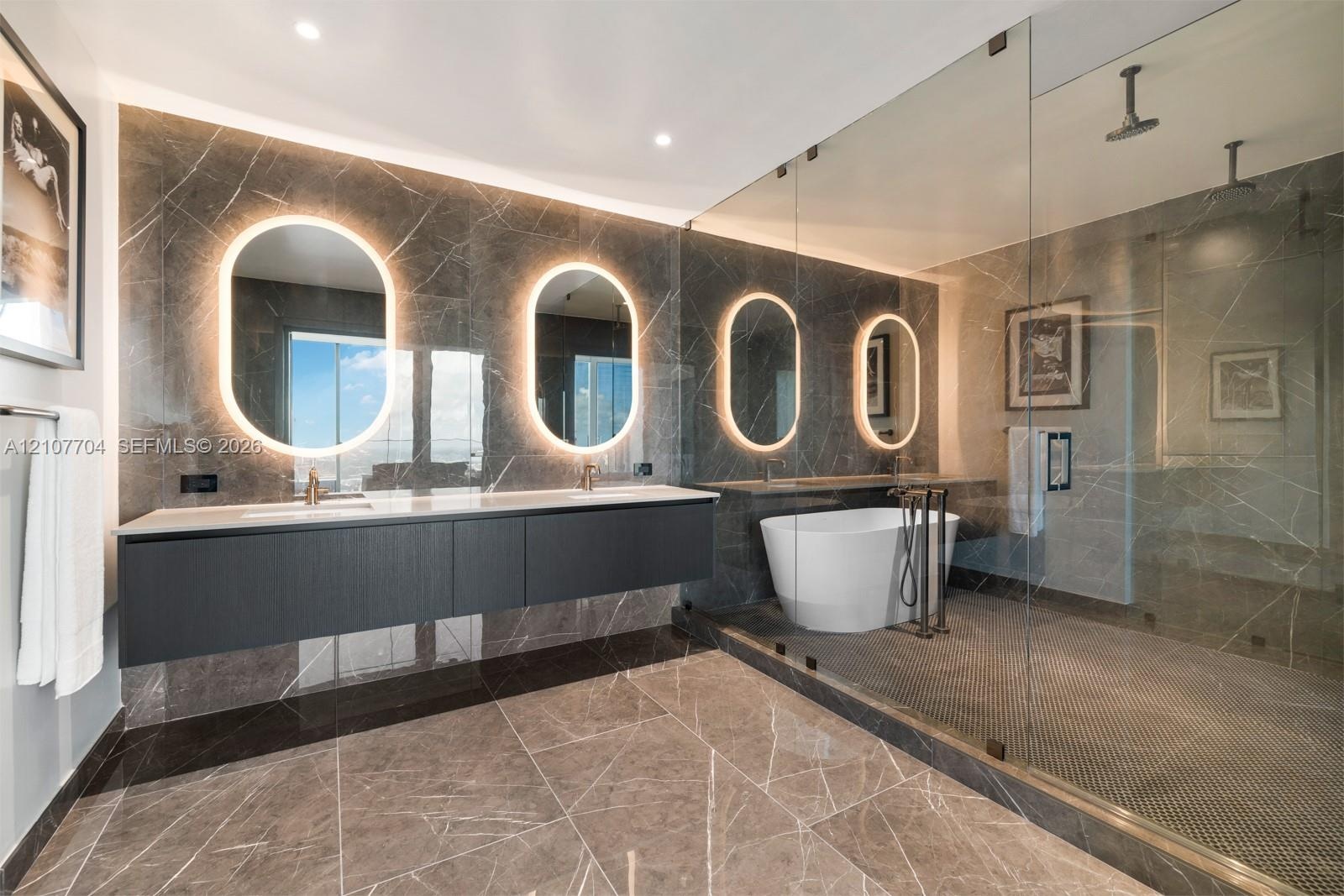 Bathroom featuring a floating double vanity with a light-toned countertop, four wall-mounted illuminated oval mirrors, a freestanding soaking tub, and