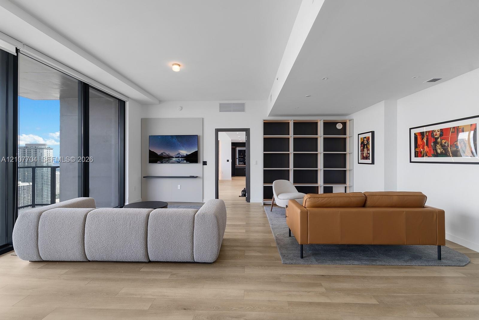 Open-concept living space featuring wood-finish flooring, floor-to-ceiling glass sliding doors, built-in floor-to-ceiling shelving, and a wall-mounted