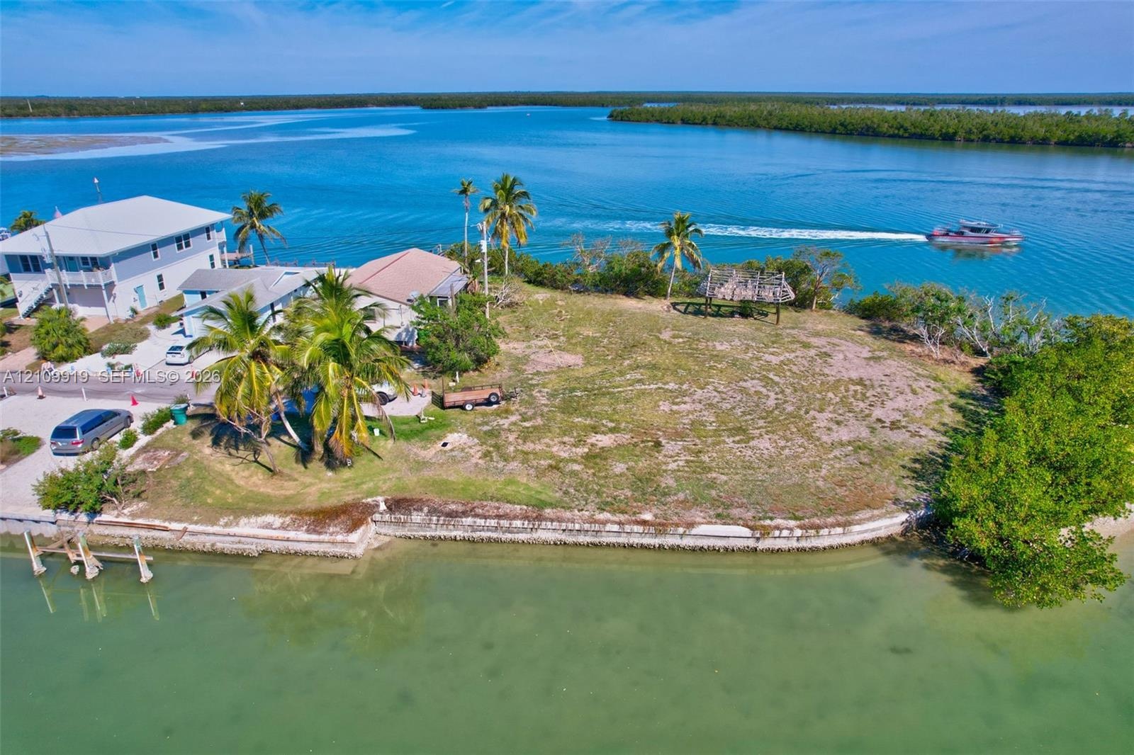 Waterfront parcel featuring direct canal access, a concrete seawall, mature palm trees, and an open-air thatch-roof structure