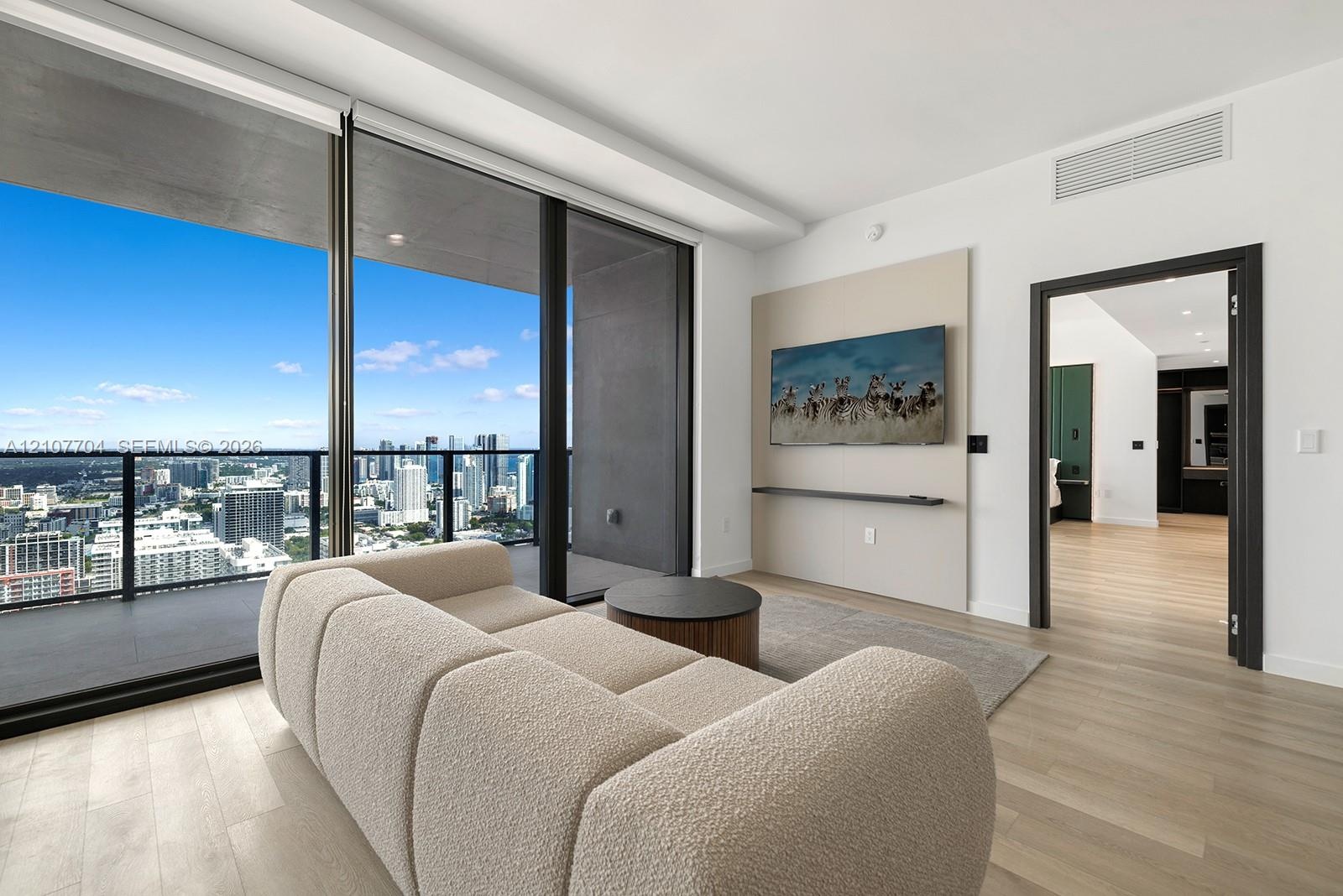 Floor-to-ceiling sliding glass doors, private balcony with metal railing, light wood-finish flooring, and a built-in wall panel with integrated shelf
