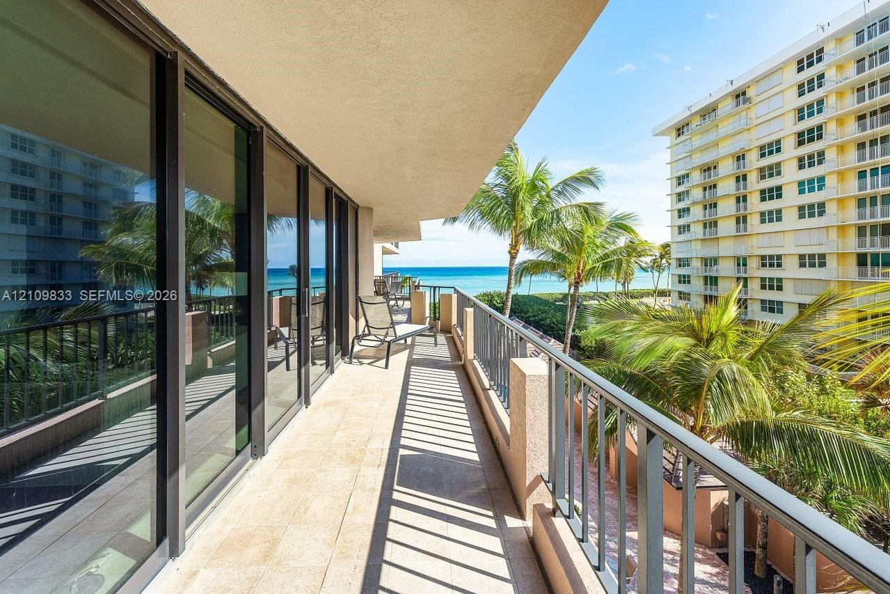 Covered balcony featuring tile flooring, full-height sliding glass doors, and metal railings with water and palm tree scenery