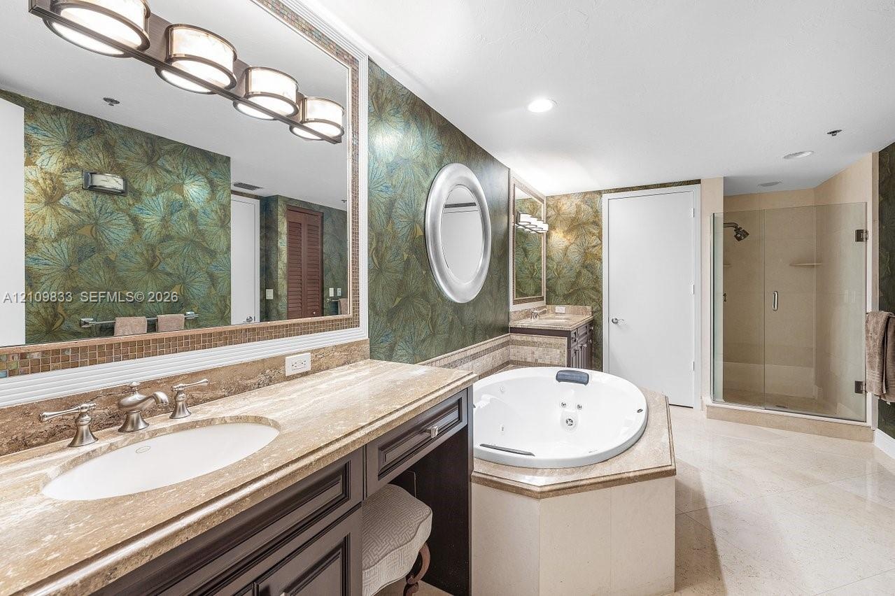Bathroom featuring a stone-topped vanity with undermount sink, jetted soaking tub, glass-enclosed shower, decorative wall coverings, and integrated li