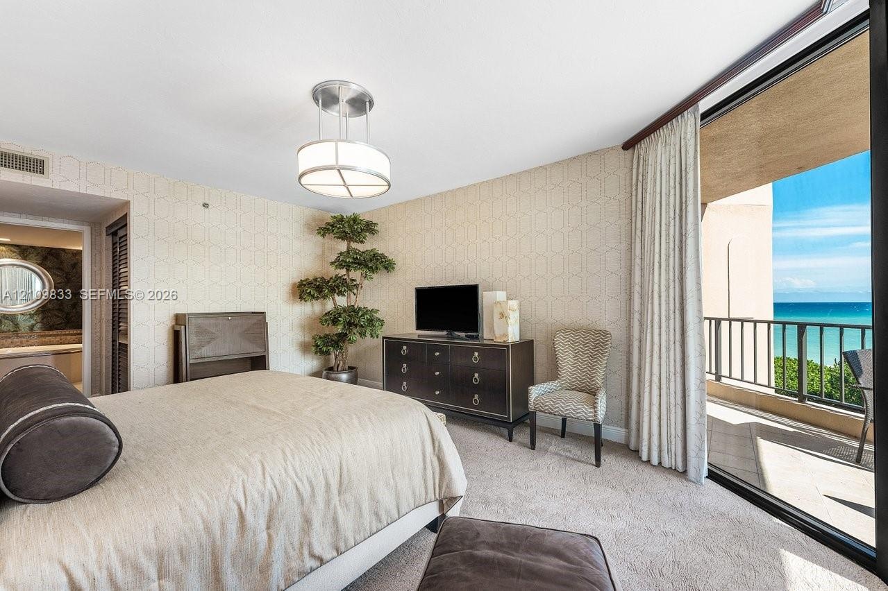 Textured wallcoverings, neutral carpeting, contemporary drum-style ceiling fixture, and full-height sliding glass doors leading to a private balcony w