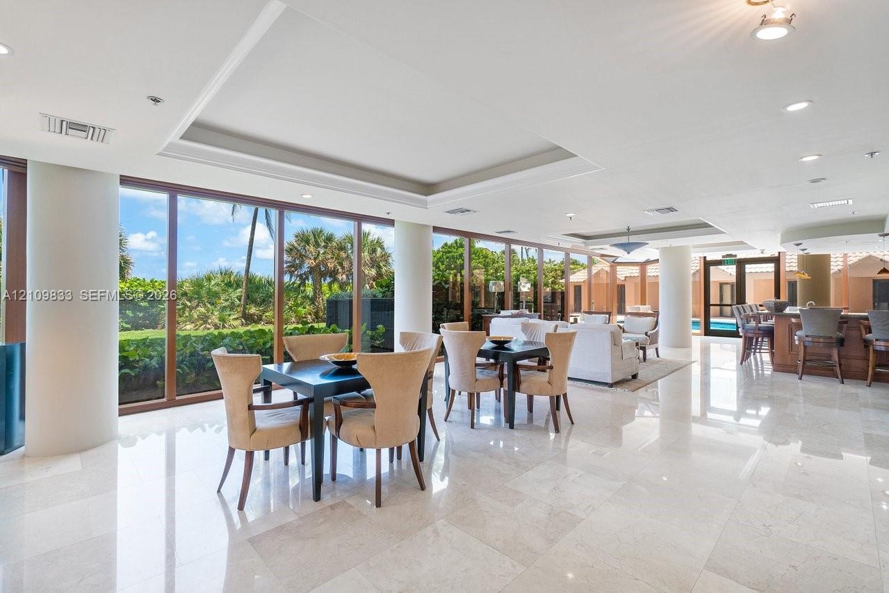 Open-concept interior featuring polished stone flooring, recessed tray ceilings, floor-to-ceiling windows with wood-finish frames, and a built-in wet 