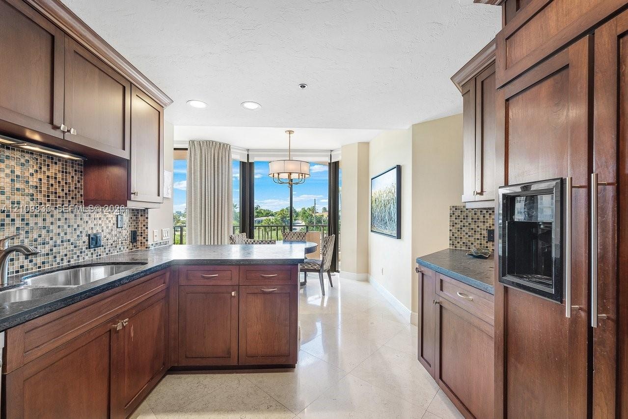 Kitchen featuring custom wood cabinetry, mosaic tile backsplash, stone countertops, recessed lighting, and tile flooring
